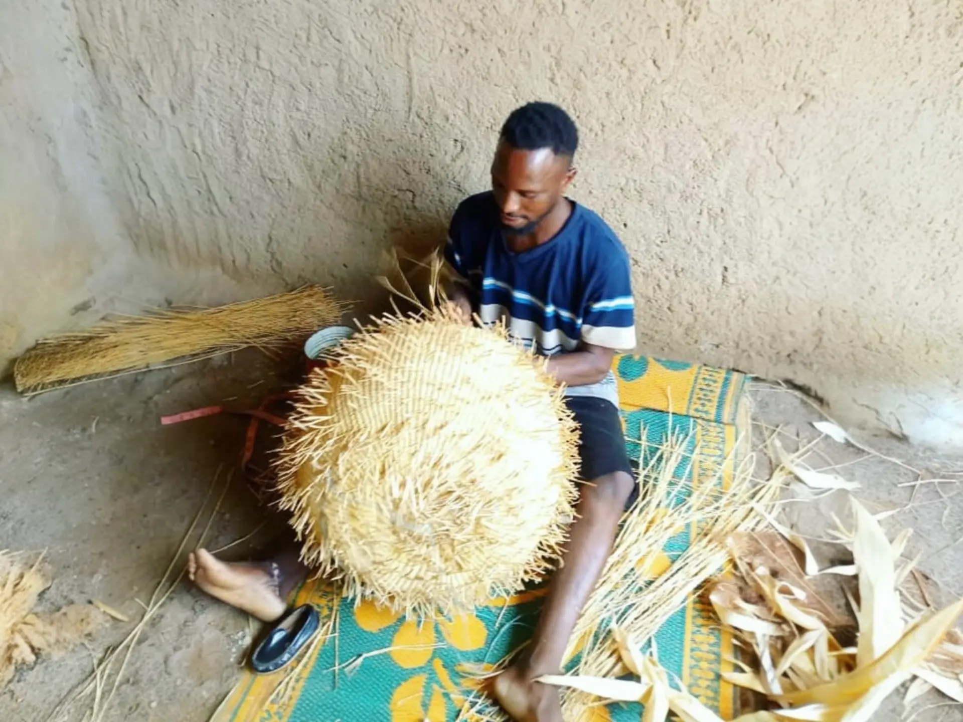 Artisan coiling dyed elephant grass cord on a woven mat