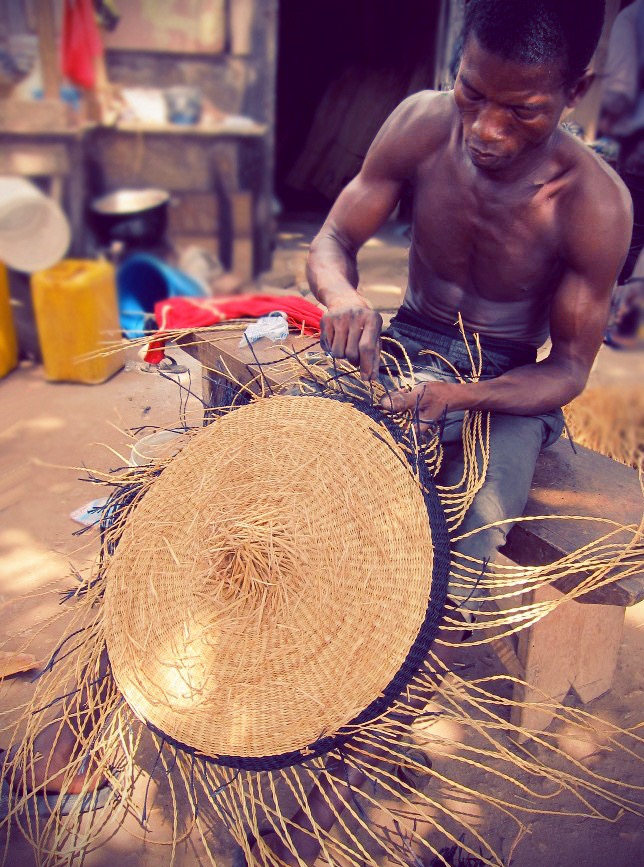 Weaver closing the flat base of a Bolga basket on her knee
